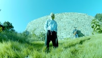 a man is standing in the grass next to a stone wall